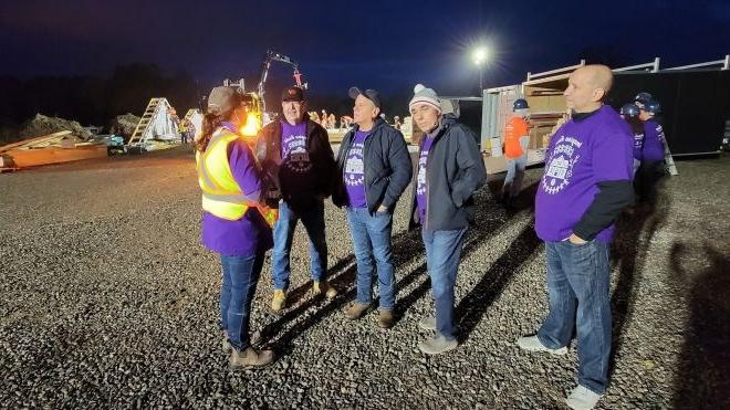 A group of people wearing purple shirts with a construction site in the background.